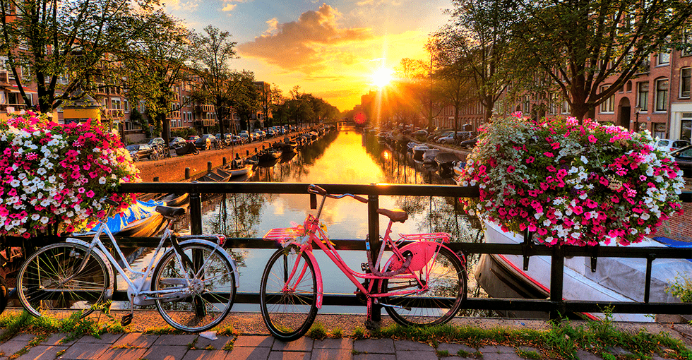kanal i Amsterdam med to sykler i forgrunnen og solnedgang i bakgrunnen